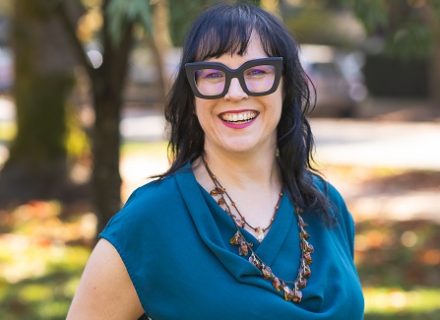 Trish Kelly, a light skinned woman with dark hair and thick black glasses.