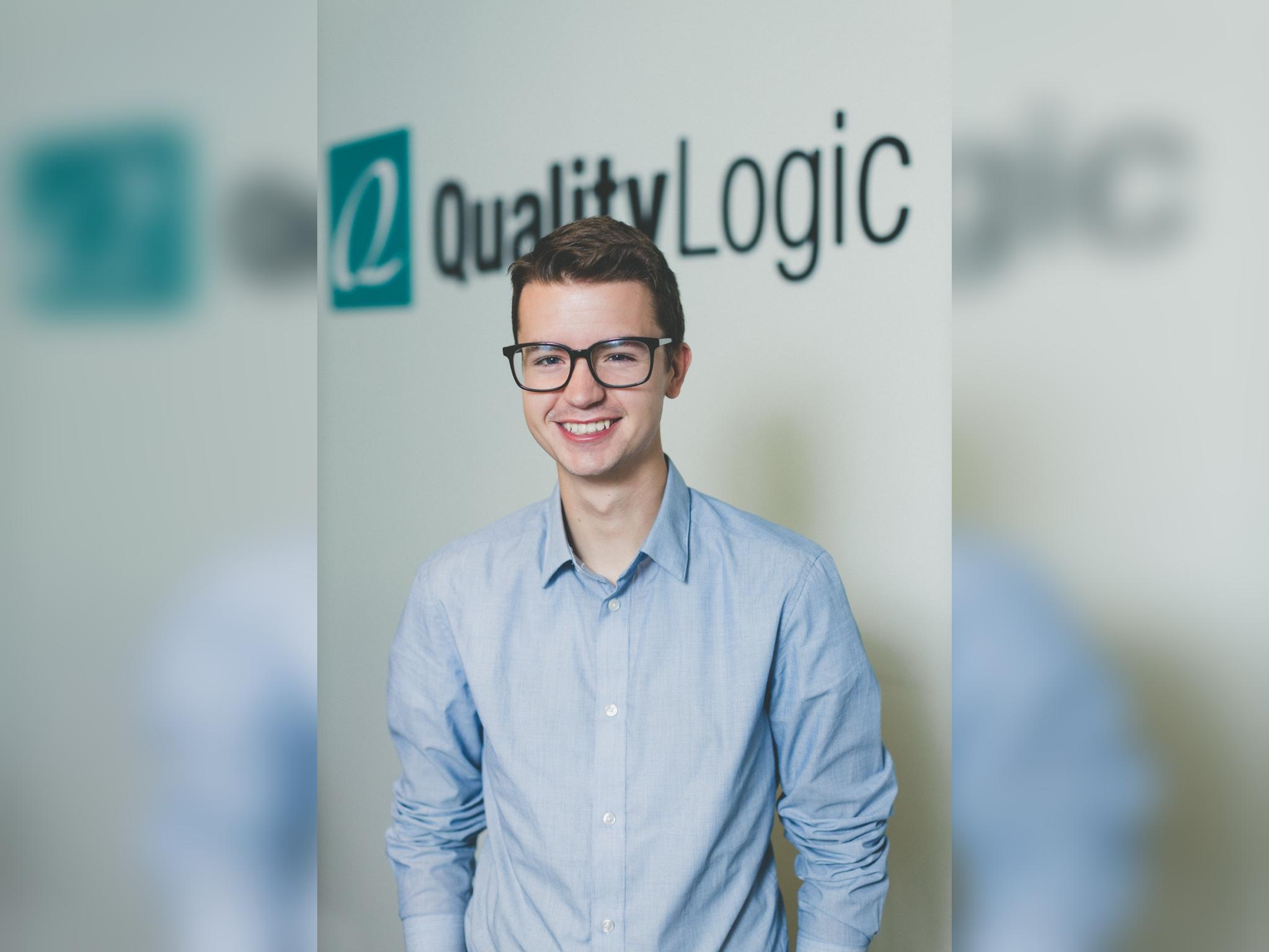 Clyde Valentine, a young man with large, dark-rimmed glasses and blue shirt, stands in front of a Quality Logic logo.