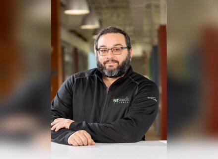 John-Marc is a gentleman with short, dark hair, glasses and a neat beard flecked with white. He's wearing a sweater branded with the WEtech Alliance logo.