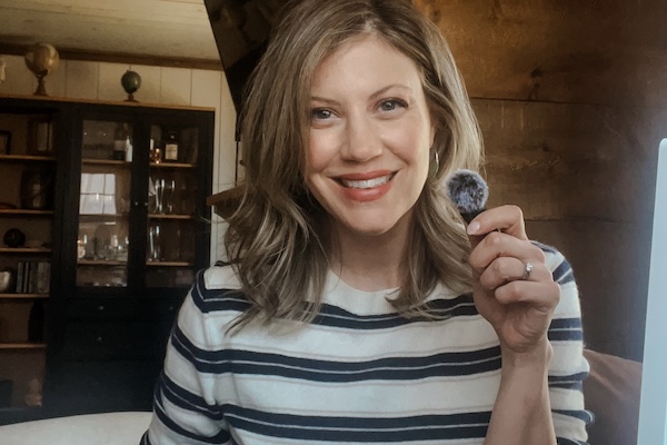 Christine Briggs is a woman with shoulder length blond hair looking into the camera.  She's wearing a striped top and holding a mic.